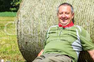 Organic farmer is resting against the hay bales