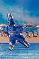 Blue starfish shape against parasols on beach