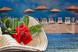 Womans summer hat with red rose with empty beach