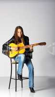 girl in black jacket and blue jeans with guitar