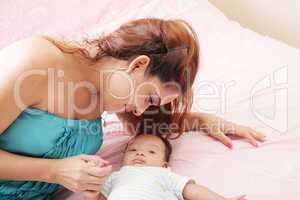 attractive mother lying with her baby on the bed at home