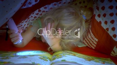 Little girl reading book under covers medium shot