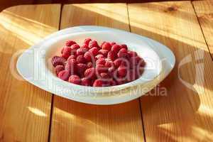 Raspberries in plate on the wooden table