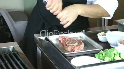 Chef salting rib eye steak before cooking