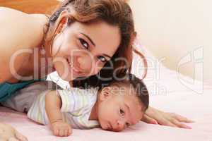 Hispanic mom lying down on bed and holding her infant son