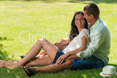 Hugging couple sitting in grass outdoors