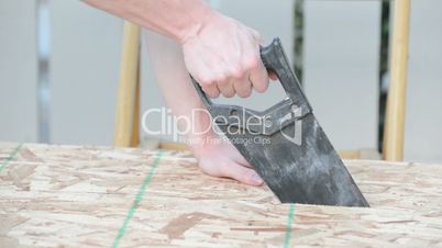 Side view of man sawing wood plank, blows dust