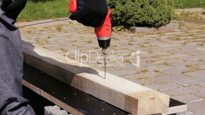 Carpenter using a screw gun to fasten screw into a wood board.