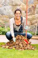 Cheerful woman sweeping leaves autumn pile backyard