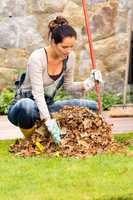 Young woman raking dry leaves autumn backyard