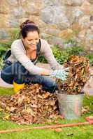 Happy woman putting dry leaves bucket yard