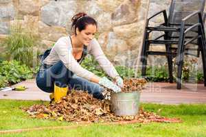 Smiling woman stuffing leaves pail autumn gardening