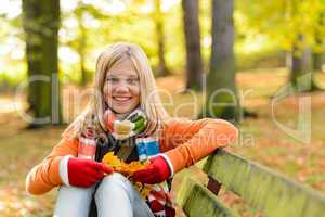 Smiling teenager girl sitting autumn park bench