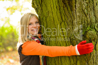 Smiling teenager girl embracing tree autumn woods