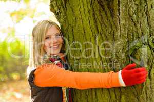 Smiling teenager girl embracing tree autumn woods