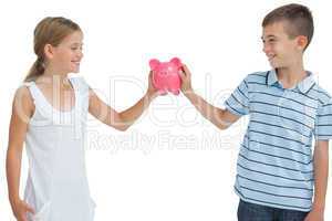 Smiling brother and sister holding piggy bank together