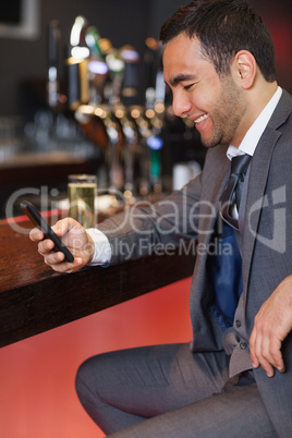 Smiling businessman sending a text while having a drink