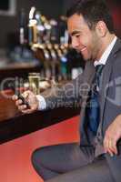 Smiling businessman sending a text while having a drink