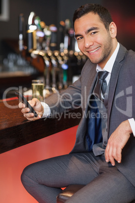 Cheerful businessman sending a text while having a drink