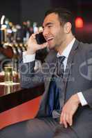 Cheerful businessman on the phone having a drink
