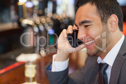 Cheerful handsome businessman on the phone having a drink