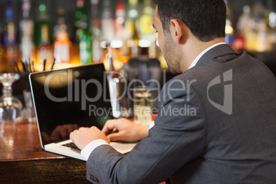 Handsome businessman working on his laptop while having a drink