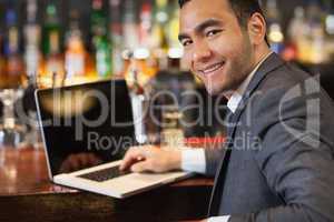 Smiling businessman working on his laptop while having a drink