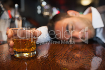 Drunk businessman with whiskey in his hand lying on a counter