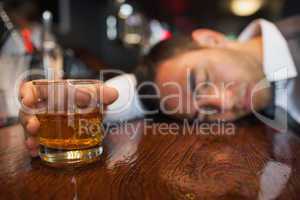 Drunk businessman with whiskey in his hand lying on a counter