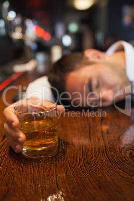 Drunk businessman holding whiskey lying on a counter