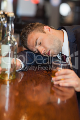 Drunk businessman holding whiskey glass lying on a counter