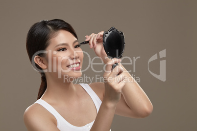 female asian applying eye liner with mirror