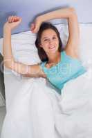 Brunette woman stretching and smiling in bed