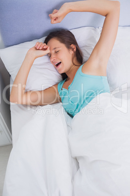Well rested brunette woman stretching and yawning in bed