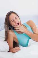 Tired woman yawning sitting on her bed