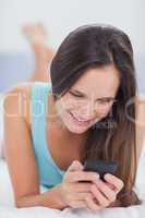 Woman using her phone and smiling while on the bed