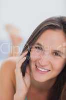 Happy woman lying on bed talking with phone