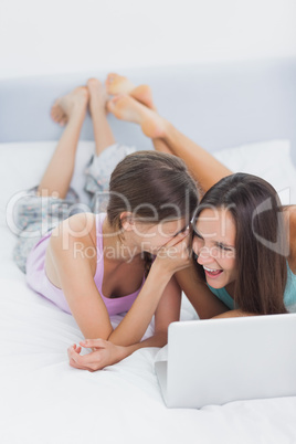 Friends lying in bed in pajamas with laptop