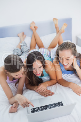 Happy friends on bed using laptop