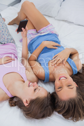 Two girls lying on bed and using phone
