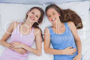 Smiling friends lying in bed and looking at camera