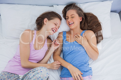 Girls wearing pajamas lying in bed and laughing