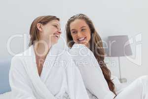 Happy friends wearing bathrobe sitting on bed