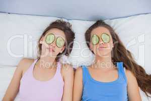 Friends relaxing in bed with cucumber on eyes