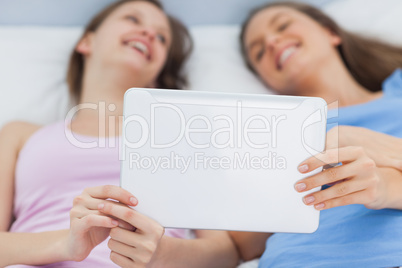 Friends resting in bed holding laptop