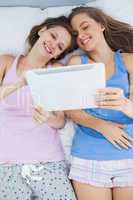 Smiling girls lying in bed holding tablet