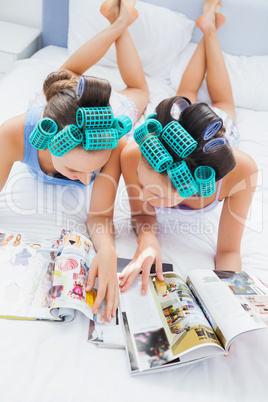 Girls in hair rollers lying in bed and reading