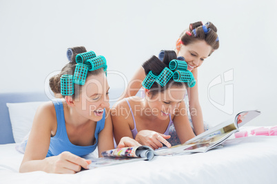 Girls wearing pajamas and hair rollers sitting in bed with magaz