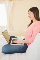 Smiling girl using a laptop sitting on her bed