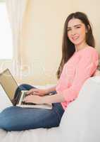 Smiling girl looking at camera using a laptop sitting on a bed